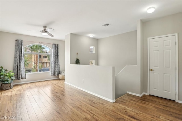 empty room featuring ceiling fan, wood finished floors, visible vents, and baseboards