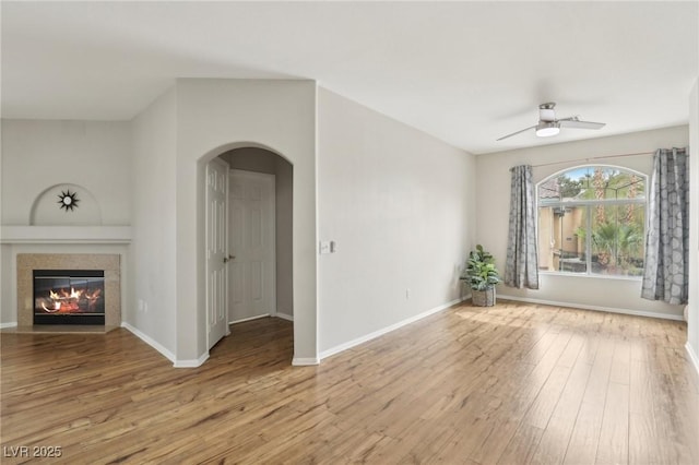 unfurnished living room with ceiling fan, arched walkways, wood finished floors, and a fireplace