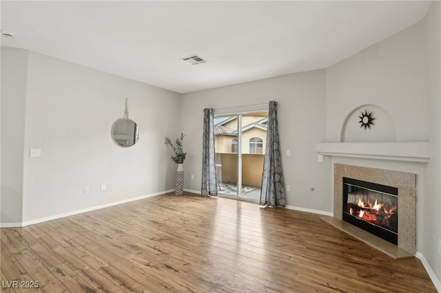 unfurnished living room with visible vents, a fireplace, baseboards, and wood finished floors