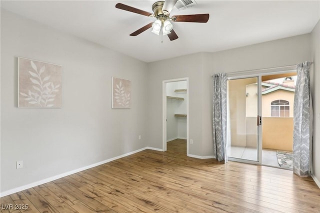 unfurnished bedroom with ceiling fan, a walk in closet, baseboards, and wood-type flooring