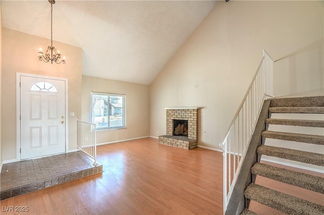 foyer entrance featuring wood finished floors, baseboards, stairs, a brick fireplace, and a chandelier