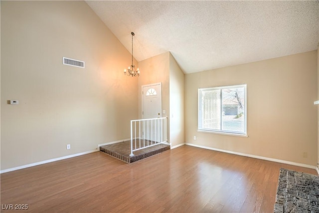 interior space featuring visible vents, a textured ceiling, wood finished floors, an inviting chandelier, and baseboards