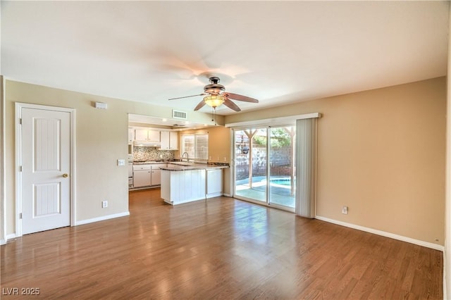 unfurnished living room with dark wood-style floors, visible vents, baseboards, and a ceiling fan