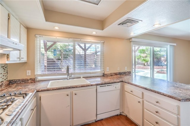 kitchen featuring visible vents, stainless steel gas cooktop, a peninsula, white dishwasher, and a sink