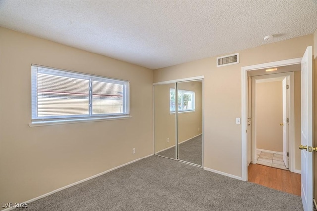 unfurnished bedroom with baseboards, visible vents, a closet, a textured ceiling, and carpet flooring