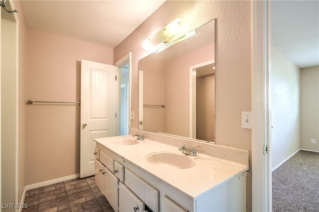 bathroom with double vanity, stone finish floor, baseboards, and a sink