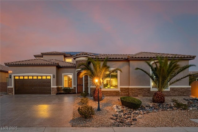 mediterranean / spanish home featuring solar panels, stucco siding, concrete driveway, a garage, and stone siding