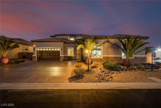 mediterranean / spanish house with an attached garage, concrete driveway, stone siding, a tiled roof, and stucco siding