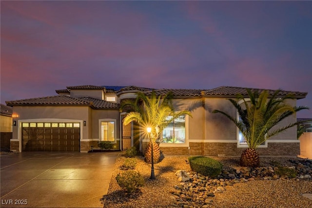 mediterranean / spanish house featuring an attached garage, concrete driveway, stone siding, a tiled roof, and stucco siding