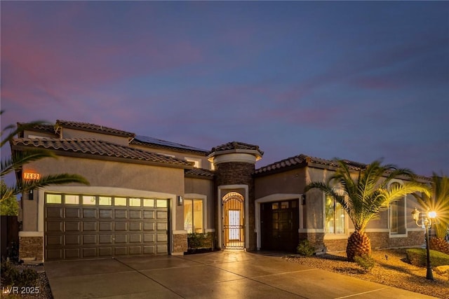 mediterranean / spanish home featuring a garage, stone siding, driveway, and stucco siding