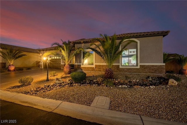 mediterranean / spanish-style house with stucco siding, concrete driveway, an attached garage, stone siding, and a tiled roof