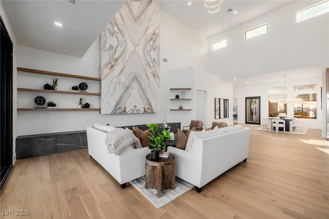 living room featuring recessed lighting, light wood-type flooring, a towering ceiling, and an inviting chandelier