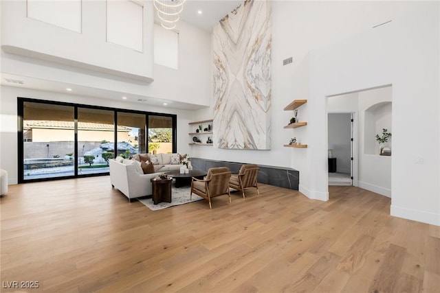 living room with light wood-type flooring, visible vents, arched walkways, and baseboards