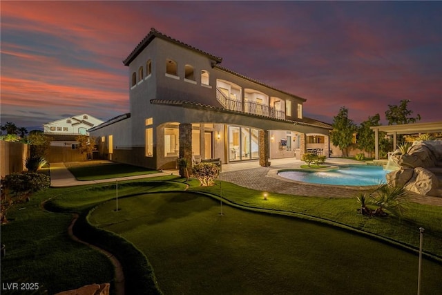 back of house at dusk with a fenced in pool, a balcony, a fenced backyard, a patio area, and stucco siding