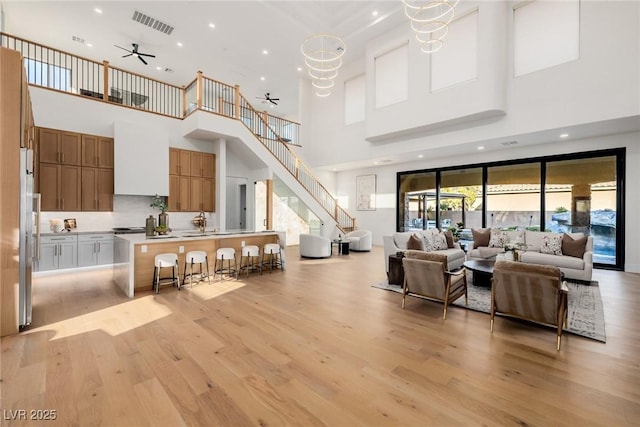 living area featuring recessed lighting, ceiling fan with notable chandelier, visible vents, stairway, and light wood finished floors