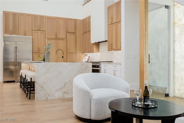 kitchen featuring light wood finished floors, an island with sink, a kitchen breakfast bar, stainless steel appliances, and light brown cabinets