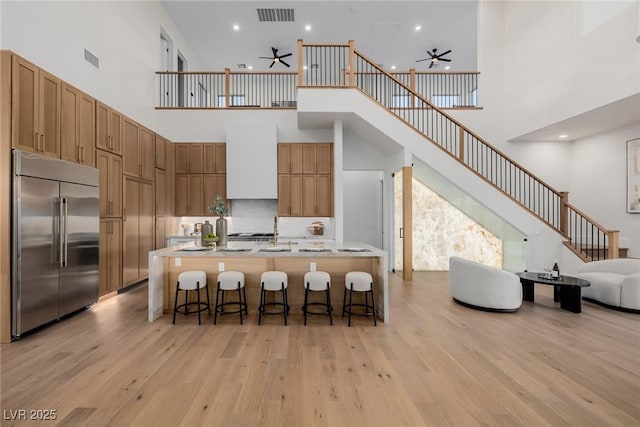 kitchen with range hood, visible vents, light wood-style flooring, a ceiling fan, and stainless steel built in refrigerator