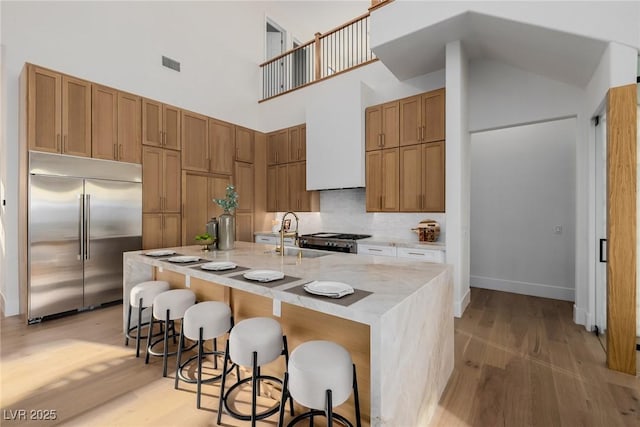 kitchen featuring light wood-style flooring, built in refrigerator, a sink, visible vents, and tasteful backsplash