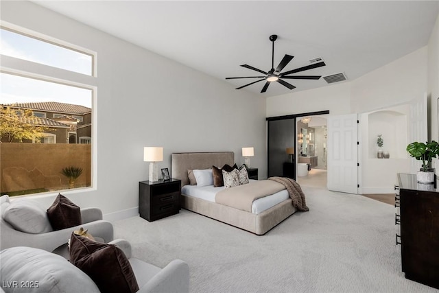 carpeted bedroom with visible vents, arched walkways, connected bathroom, baseboards, and ceiling fan