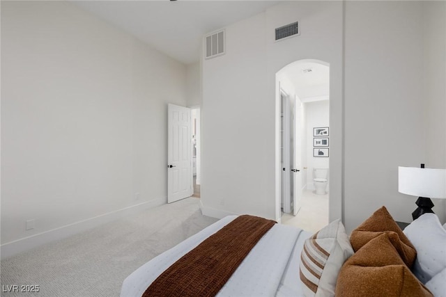 bedroom with baseboards, visible vents, arched walkways, and light colored carpet