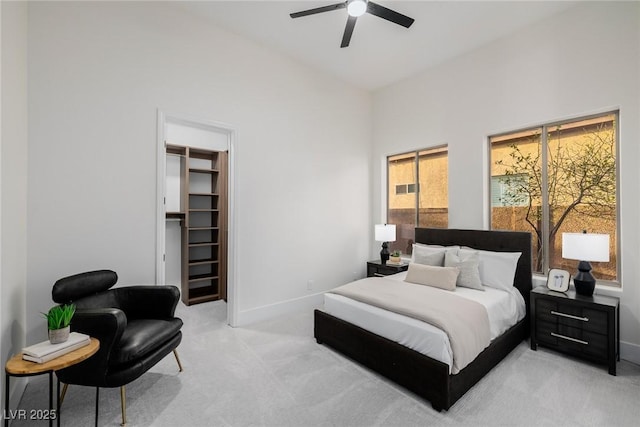 bedroom featuring ceiling fan, light carpet, baseboards, a closet, and a walk in closet