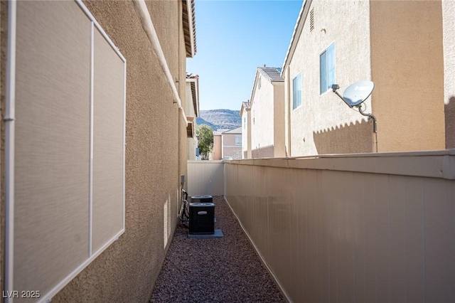 view of side of home with cooling unit, a fenced backyard, a mountain view, and stucco siding