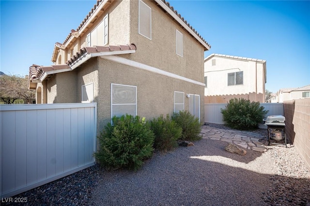 view of side of home featuring a tile roof, fence, a patio, and stucco siding