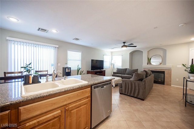 kitchen with a tile fireplace, a sink, visible vents, a ceiling fan, and dishwasher