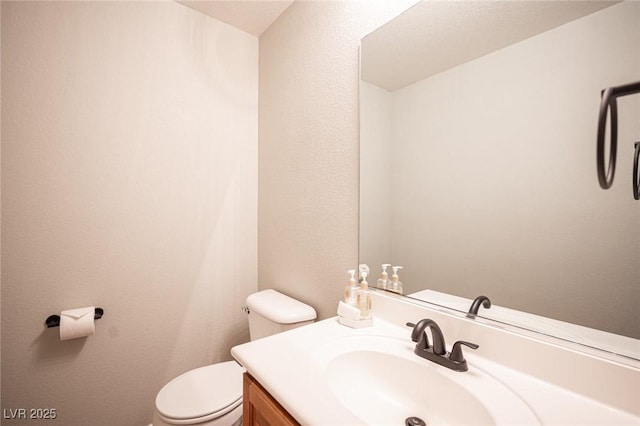 half bathroom with a textured wall, vanity, and toilet