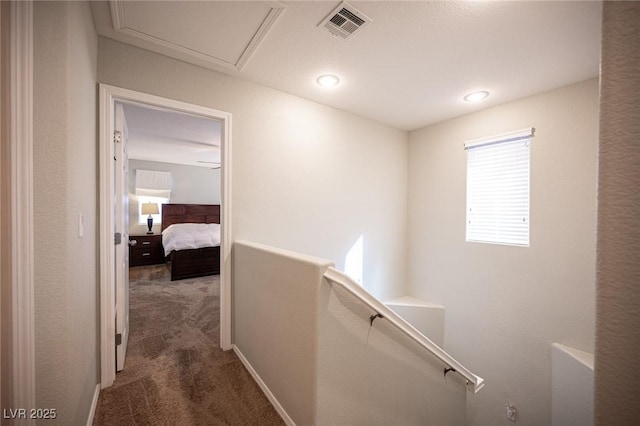 hall with attic access, visible vents, carpet flooring, and an upstairs landing