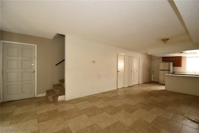 unfurnished living room with stairs, a textured ceiling, and baseboards