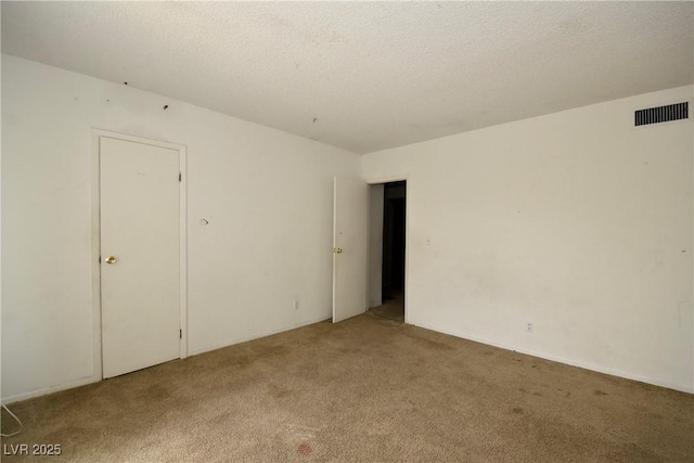 spare room featuring carpet flooring, visible vents, and a textured ceiling