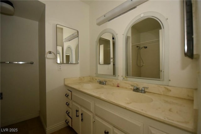 full bath with double vanity, a shower, a sink, and baseboards