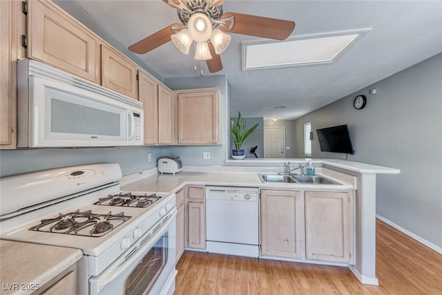 kitchen with white appliances, a peninsula, light countertops, light brown cabinetry, and a sink