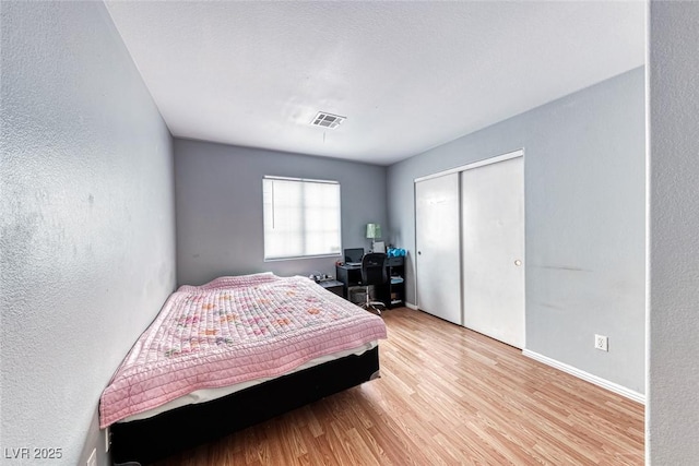 bedroom with a closet, visible vents, a textured wall, light wood-style floors, and baseboards