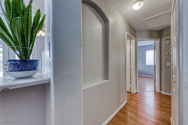 corridor with a textured wall, wood finished floors, and baseboards