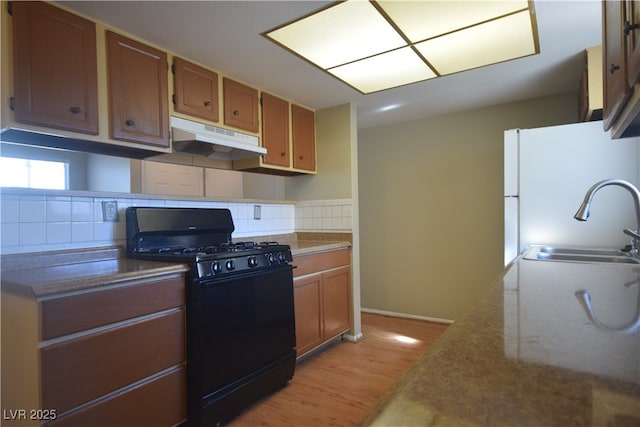 kitchen featuring under cabinet range hood, a sink, black gas stove, freestanding refrigerator, and light wood finished floors