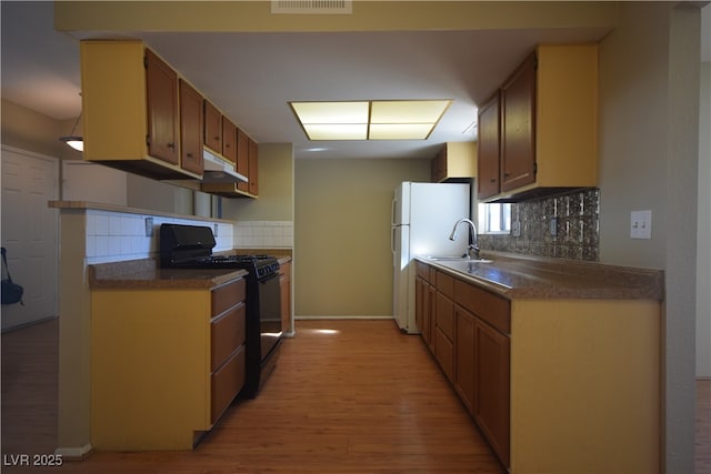 kitchen featuring black gas stove, dark countertops, light wood-type flooring, and a sink