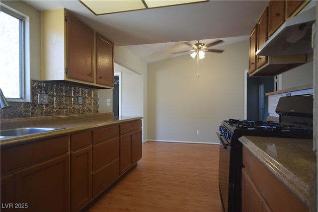 kitchen with light wood-style flooring, backsplash, black range with gas stovetop, brown cabinetry, and under cabinet range hood