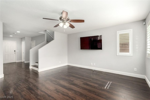 empty room featuring stairs, ceiling fan, dark wood-style floors, and baseboards