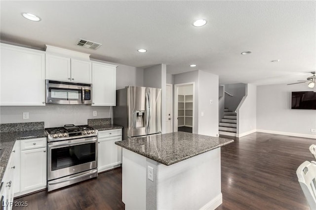 kitchen featuring visible vents, open floor plan, dark wood-type flooring, dark stone countertops, and stainless steel appliances