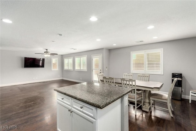 kitchen featuring recessed lighting, baseboards, a center island, dark wood-style floors, and dark countertops