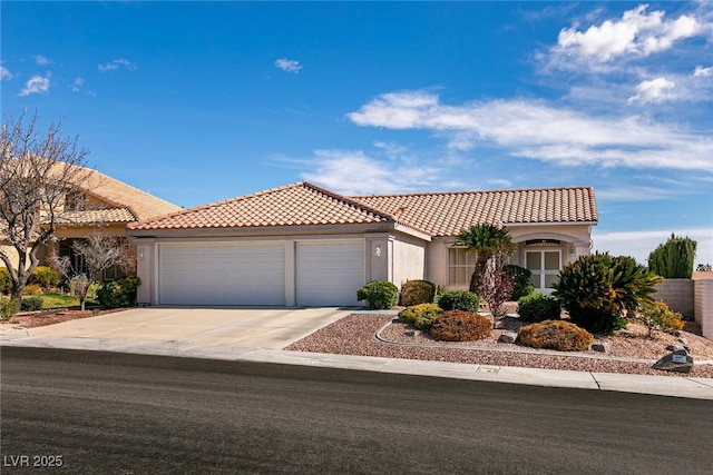 mediterranean / spanish house featuring a garage, concrete driveway, a tiled roof, and stucco siding