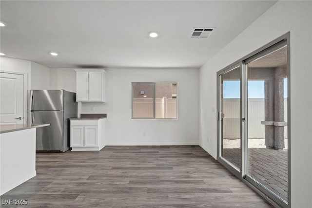 kitchen featuring visible vents, freestanding refrigerator, white cabinetry, wood finished floors, and baseboards