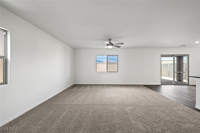 carpeted empty room with wood finished floors, a ceiling fan, and baseboards