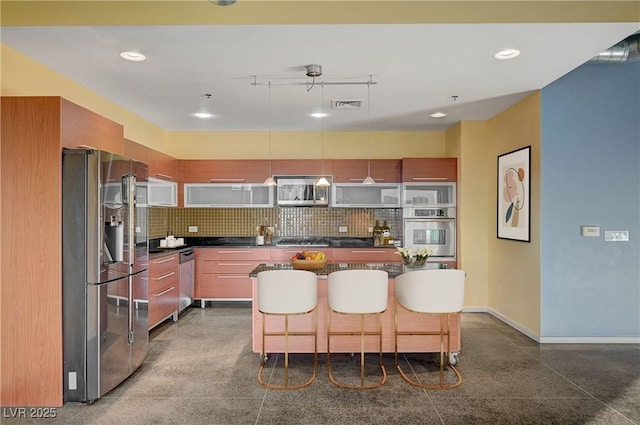 kitchen featuring dark countertops, visible vents, a breakfast bar area, decorative backsplash, and stainless steel appliances