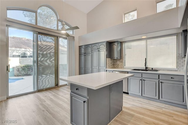 kitchen featuring a high ceiling, gray cabinets, a sink, light countertops, and stainless steel dishwasher