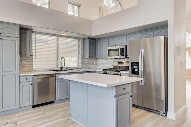 kitchen with light wood-style flooring, gray cabinets, a sink, stainless steel appliances, and light countertops