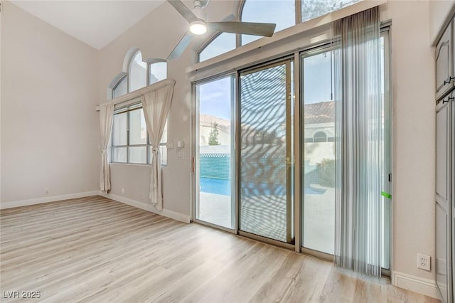 interior space featuring a ceiling fan, light wood-type flooring, baseboards, and vaulted ceiling