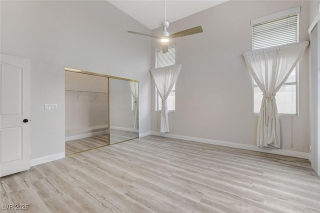 unfurnished bedroom featuring ceiling fan, baseboards, wood finished floors, a closet, and high vaulted ceiling